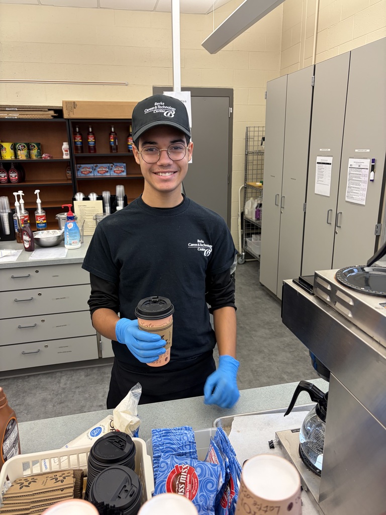 A person wearing a hat and blue gloves holds a coffee cup in a coffee shop.