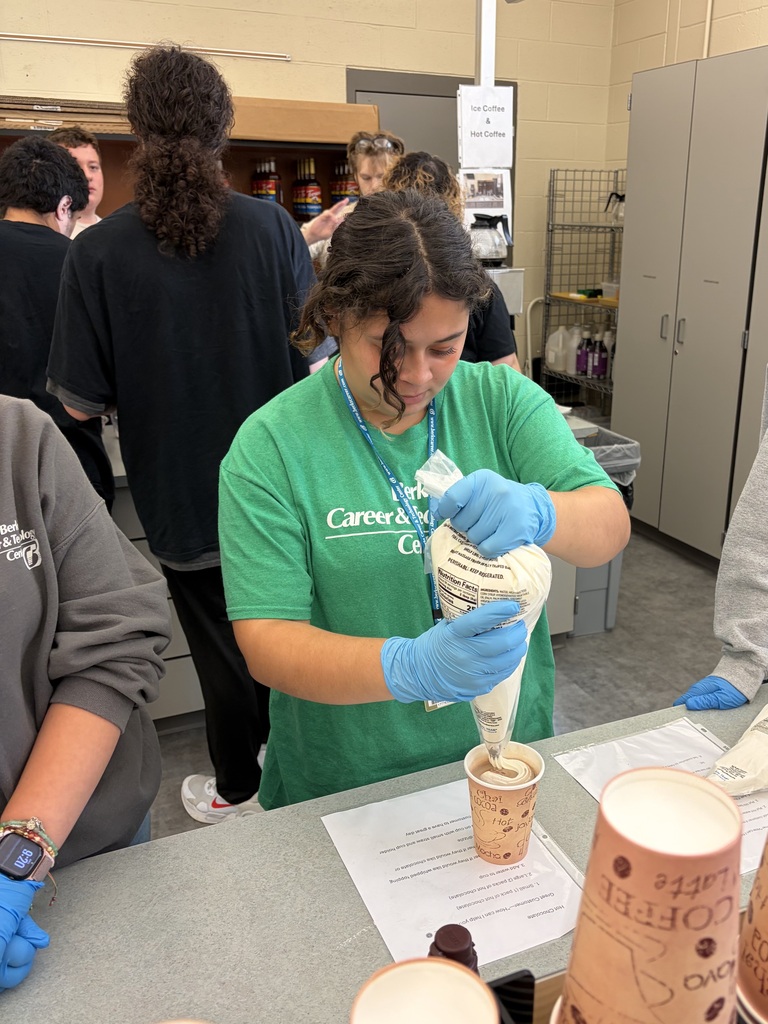 Woman in a green shirt and blue gloves fills a cup with frosting. A group of people stand behind her.