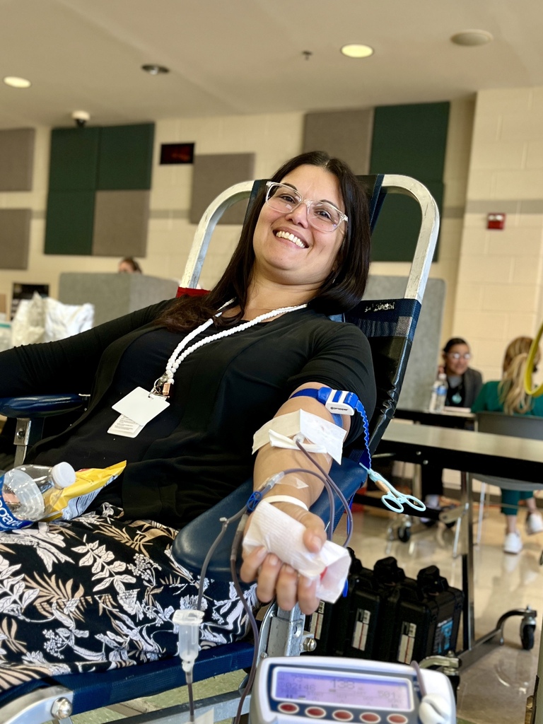 A woman sits in a chair with an IV on her arm. She smiles. Two people sit at a table behind her.