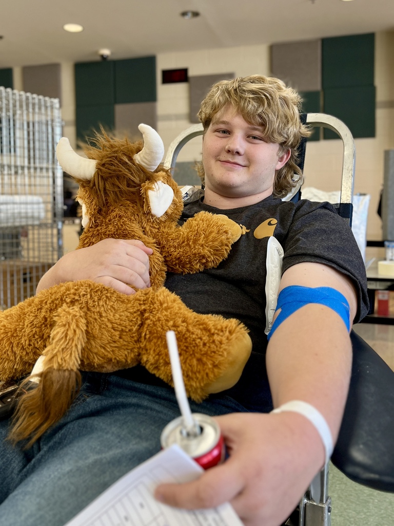 Person in wheelchair holding stuffed animal with horns and smiling, holding paper and can.