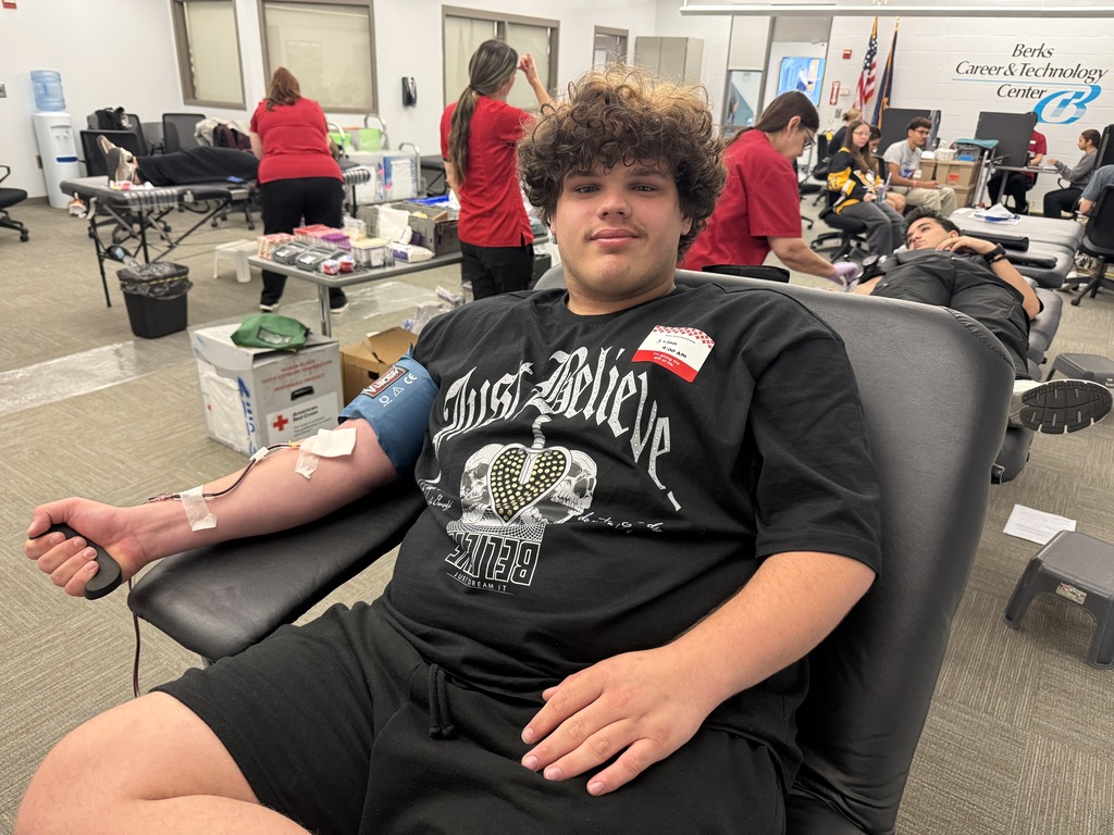 A person with an IV in their arm sits in a chair at a blood donation event.