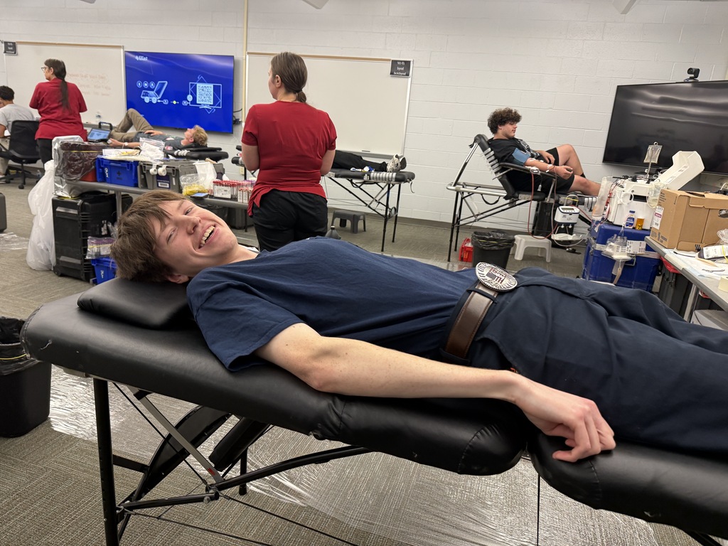 A man smiles as he lies on a massage table in a room with others working.