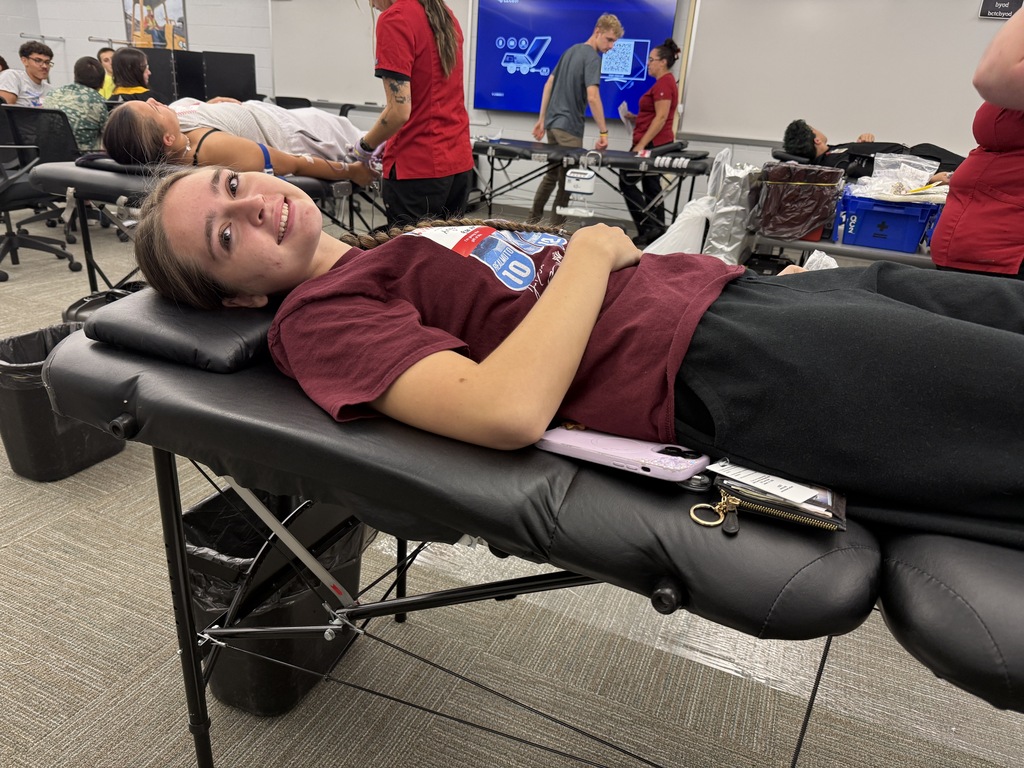 A woman lying on a massage table, smiling, while several other individuals, some lying and some standing, are nearby.