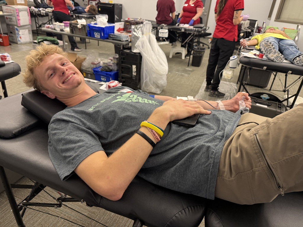 A man lies on a padded chair with his arm hooked to a blood donation device.
