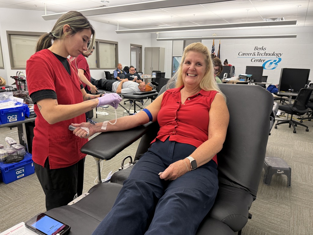 Woman sits in chair, smiling at staff. She has a blood pressure cuff on her arm.