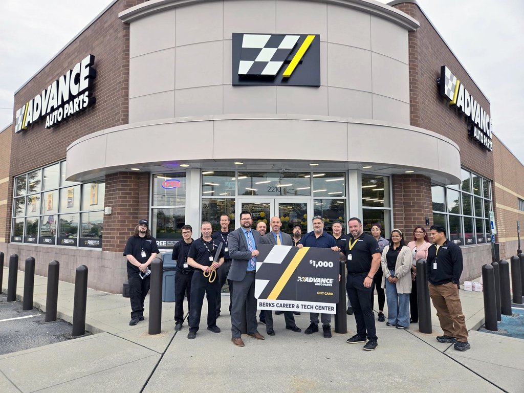 A group of people stand in front of an Advance Auto Parts store with a sign in the center.