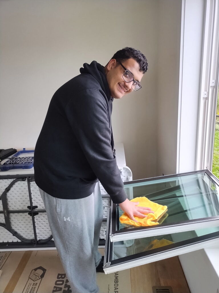 A person cleaning a glass door with a yellow cloth, standing next to a window.