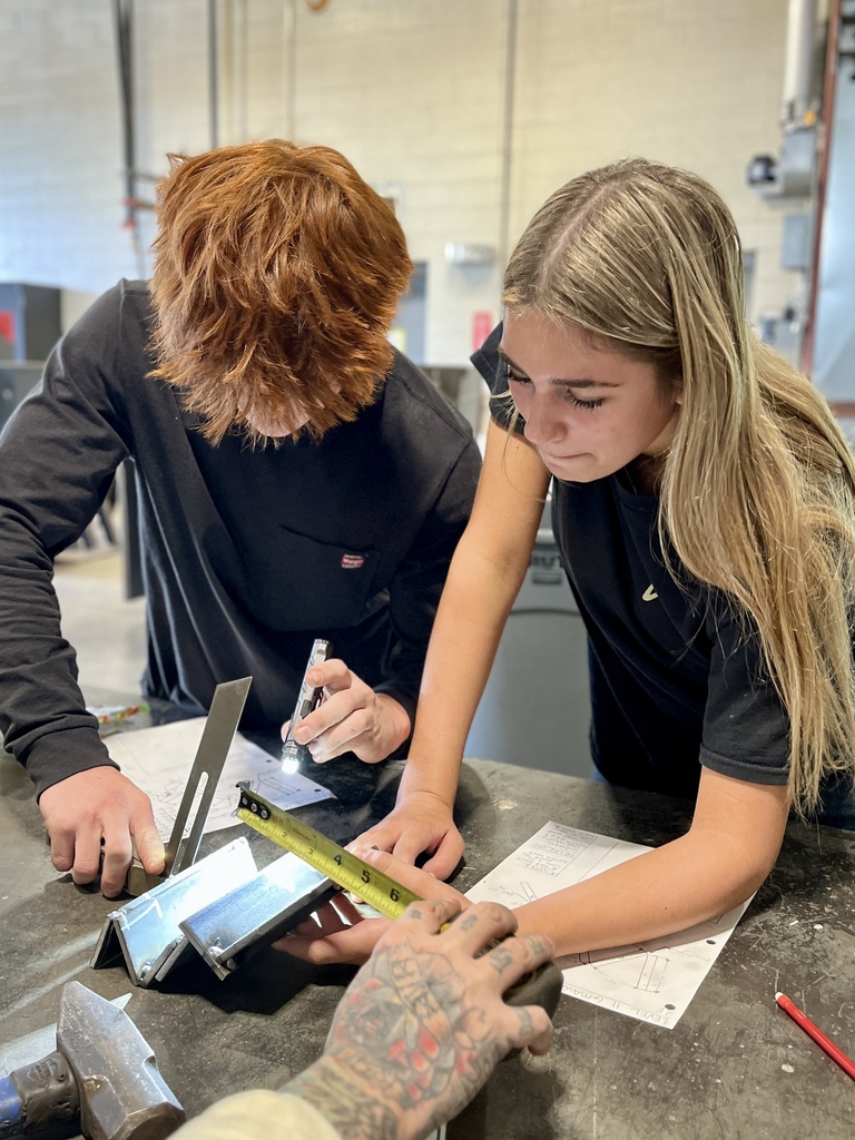 Two people are measuring a solar panel on a table, with tools and papers around them.