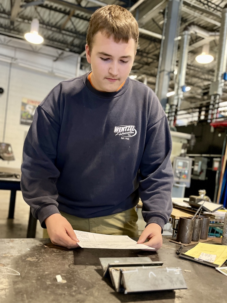 A young man in a blue sweatshirt reads a document on a table in a large room.