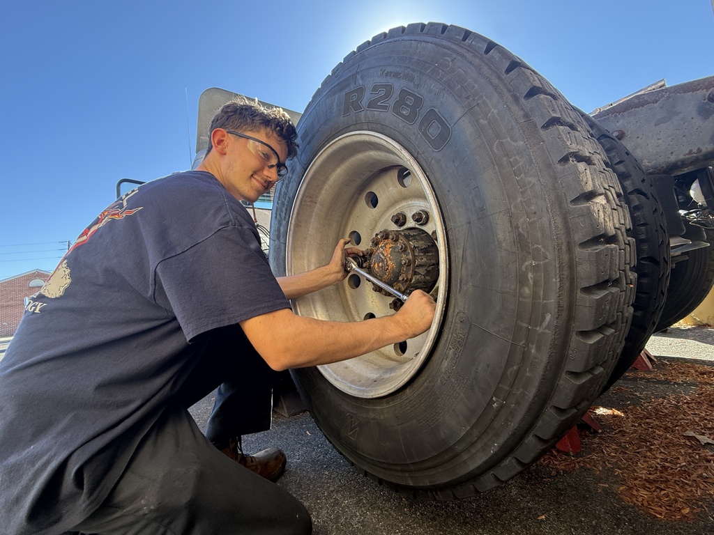 A man in a blue shirt uses a wrench to change a tire on a vehicle.