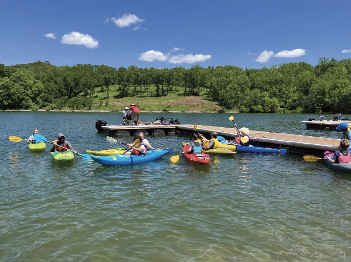 Students kayaking in the water next to a small dock on a sunny day.