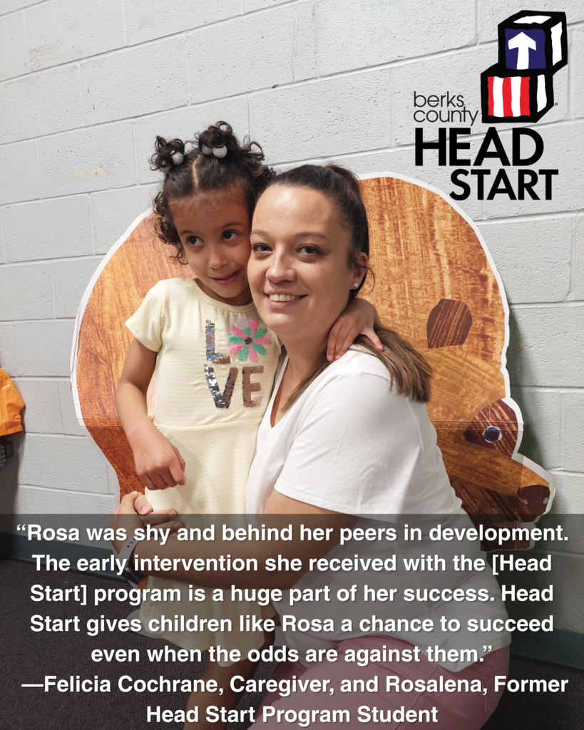 A caregiver and child pose together in front of a decorative background at a Berks County Head Start event. The child, Rosalena, wears a yellow shirt with the word "LOVE" on it and rests her arm around her caregiver, Felicia Cochrane, who is smiling at the camera. A quote overlays the image, highlighting their positive experience with Head Start: “Rosa was shy and behind her peers in development. The early intervention she received with the [Head Start] program is a huge part of her success…” The Berks County Head Start logo is displayed in the top right corner.