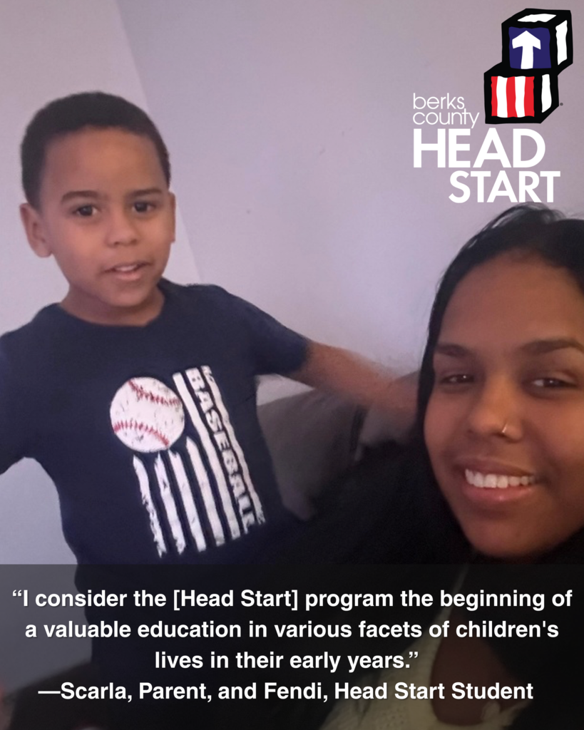A medium shot of a young,  boy on the left, looking directly at the camera with a slight smile. He is wearing a dark blue t-shirt with a white baseball and vertical stripes, resembling a flag. To his right and slightly behind him is a woman with dark hair, also looking towards the camera with a friendly expression. Her hair is down, and she has a small nose ring. In the top right corner is the Berks County Head Start logo, featuring a blue and white block with a red upward arrow. A quote at the bottom of the image reads: "I consider the [Head Start] program the beginning of a valuable education in various facets of children's lives in their early years." —Scarla, Parent, and Fendi, Head Start Student.