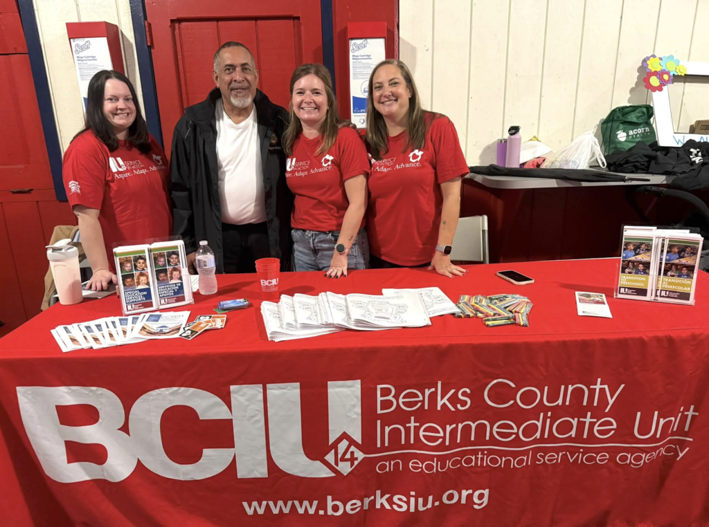 Group of staff standing in front of a red BCIU Berks County Intermediate Unit tablecloth