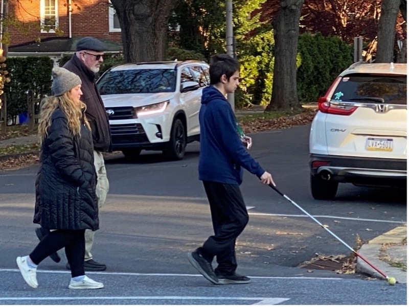 Visually-impaired student being observed by teachers crossing the street