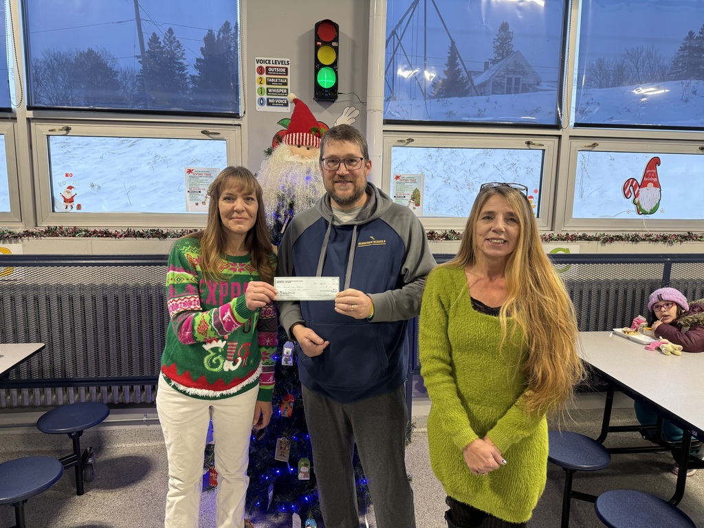 two women providing donation check to a gentlemen in front of a Christmas tree
