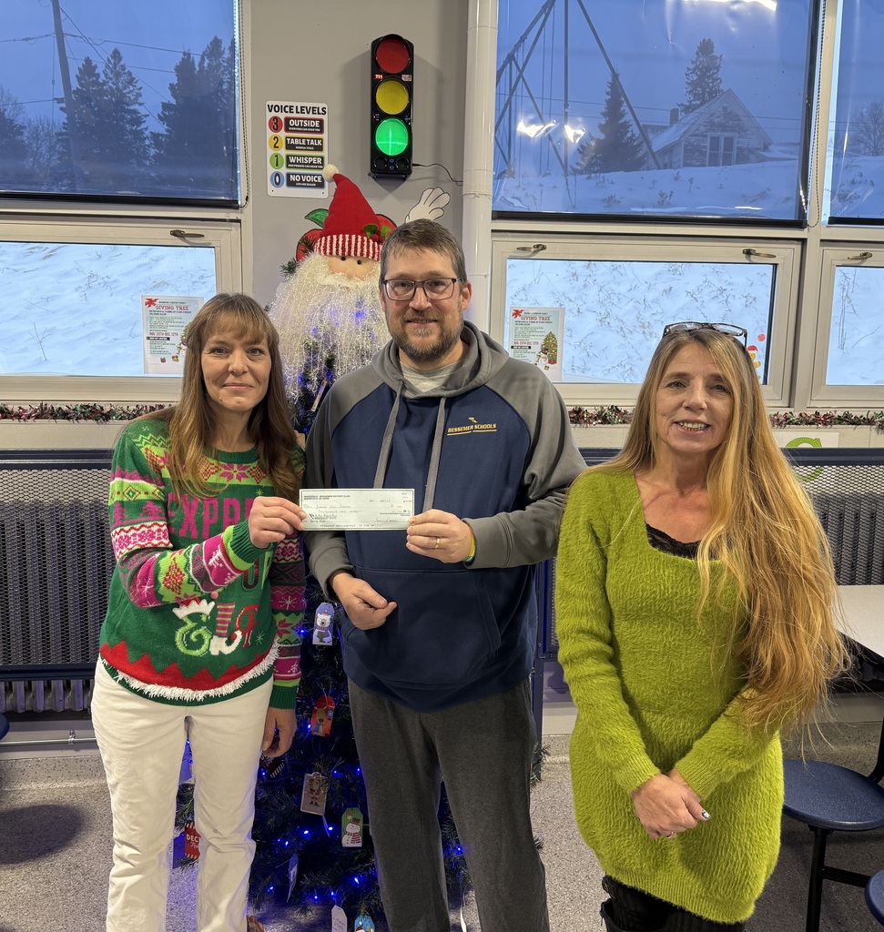 two women donating a check to a man in front of a Christmas tre