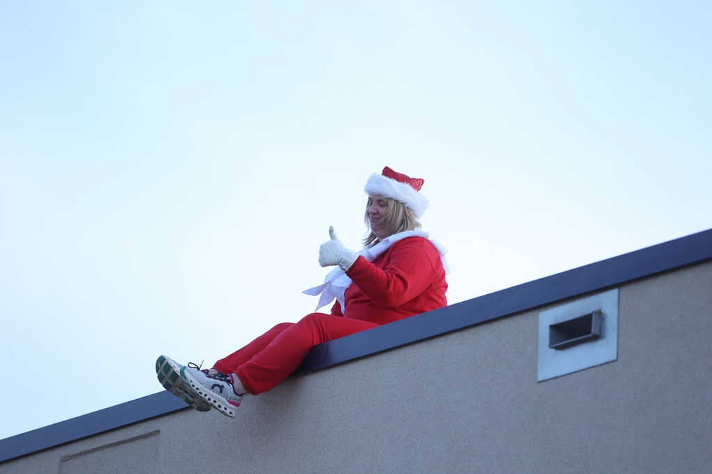principal sitting on the roof in elf costume, giving a thumbs up to students