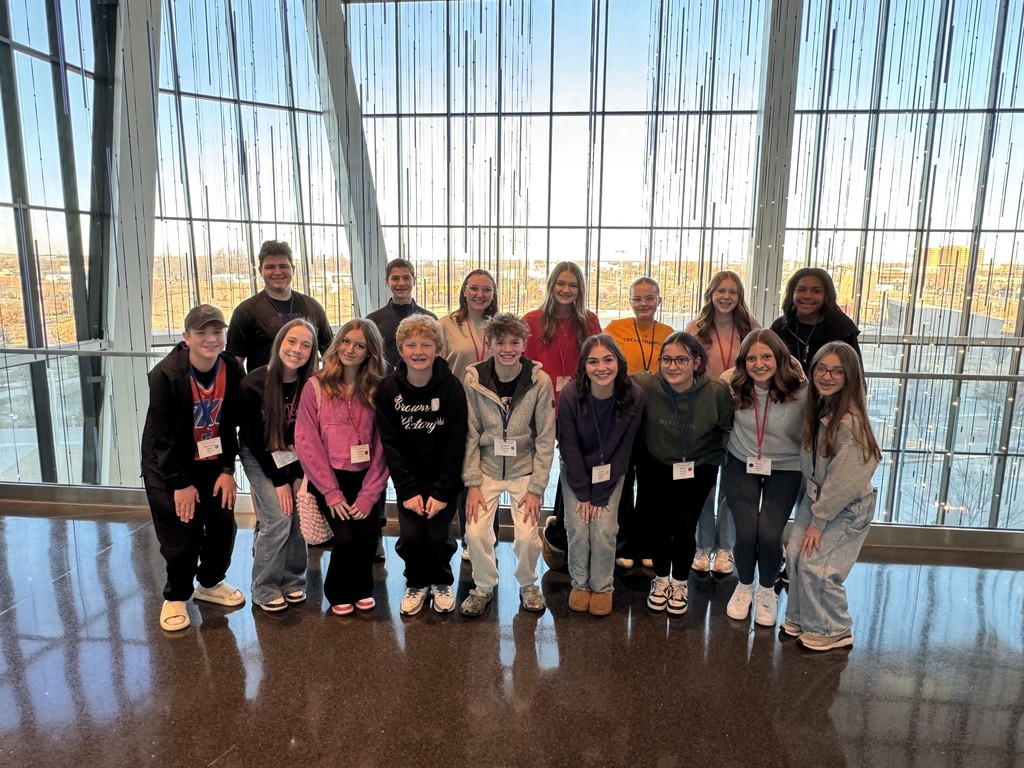 photo of sixteen choir students in front of a glass window