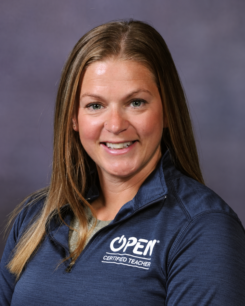Professional headshot of Coach Erin Wright smiling against a muted purple-gray background. She has long brown hair with blonde highlights and is wearing a navy quarter-zip top embroidered with the white βOPEN Certified Teacherβ logo.