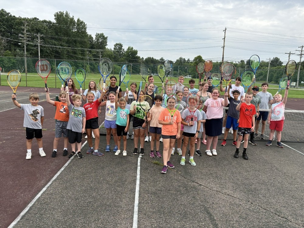 Students holding up their tennis rackets while standing on a tennis court