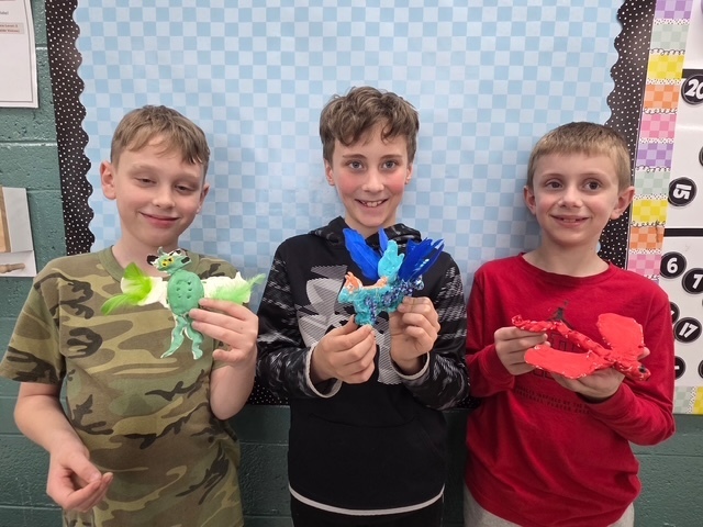 3 students holding their science art projects