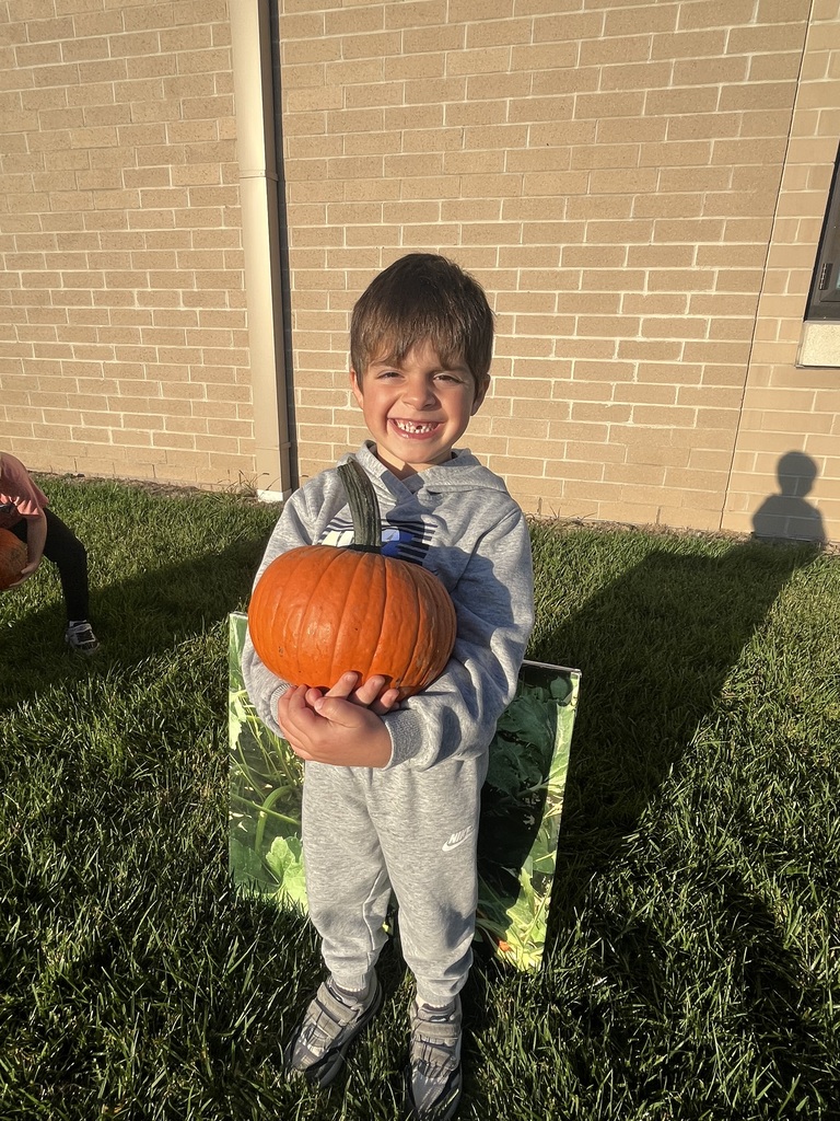 A boy in a grey sweatsuit smiling holding a pumpkin