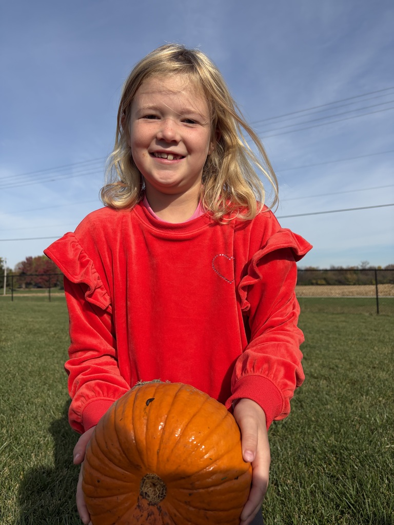 a close up photo of a girl in a red shirt holding a pumpkin