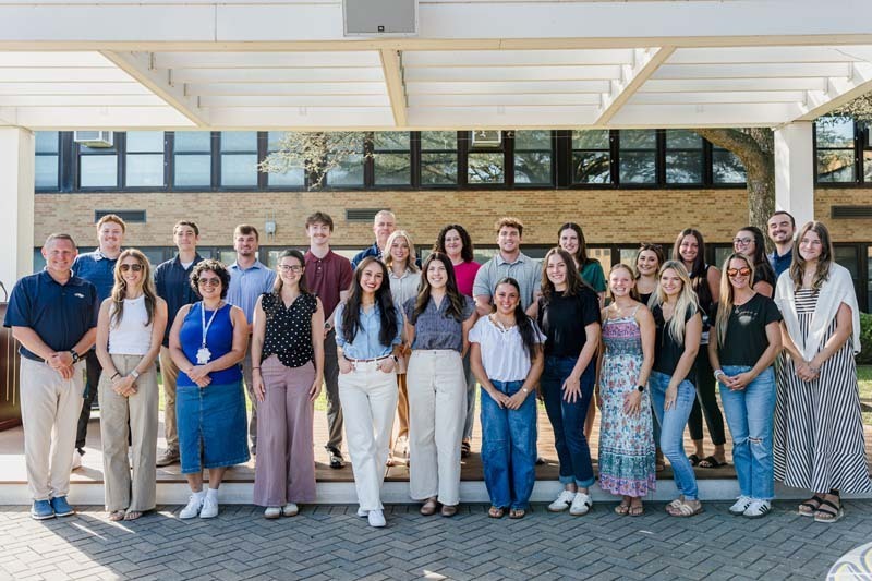 Group photo of new teachers outside school building.