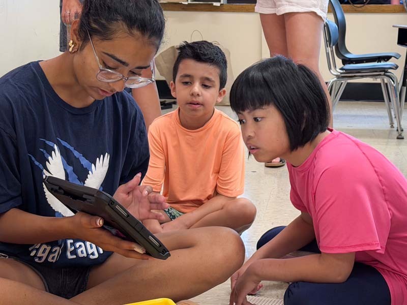 Students sitting on the floor, reading off of tablet.