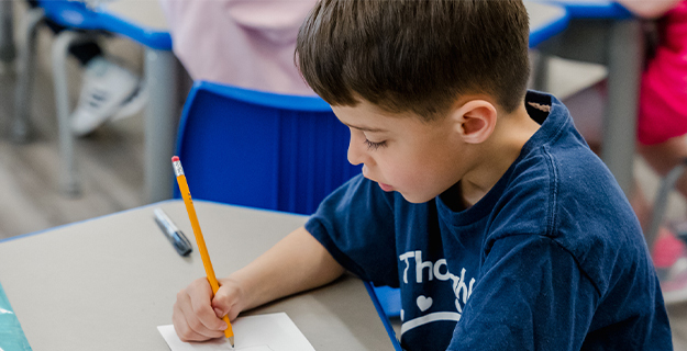 Student writing on paper with pencil.