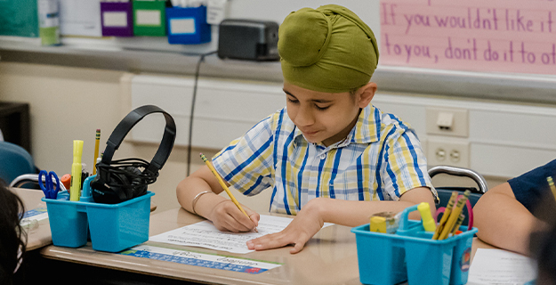 Student writing on paper at desk.