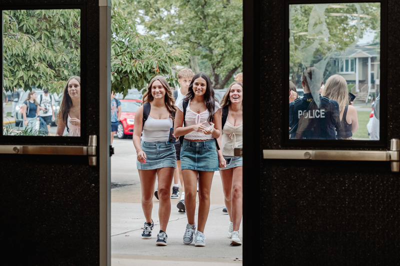 High school students smiling and walking through doors, enjoying a sunny day outside.
