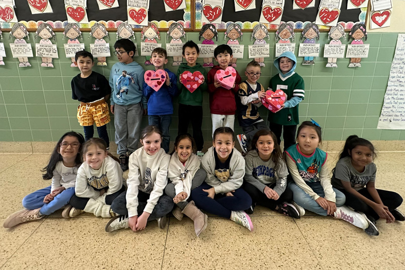 A group of young children and a teacher pose in a decorated school hallway.