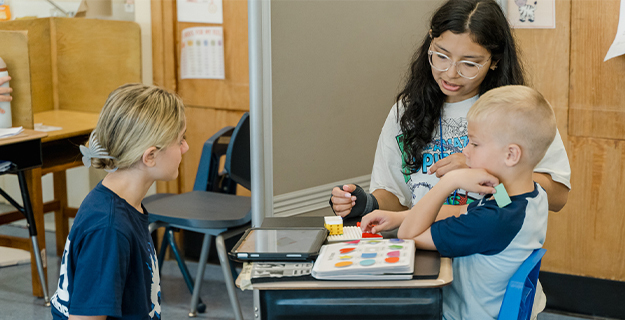 Older students helping younger student with book.