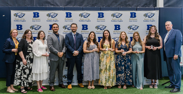 Group photo of award recipients at Bethpage High School ceremony, featuring faculty and staff in front of the school's banner.