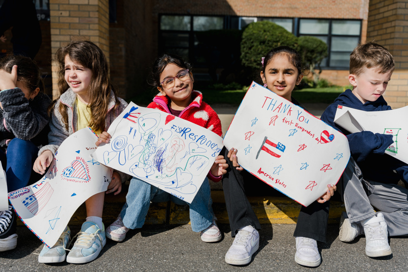 Children holding handmade signs expressing gratitude for first responders during a community event.