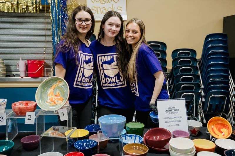 Students standing in front of painted bowls.