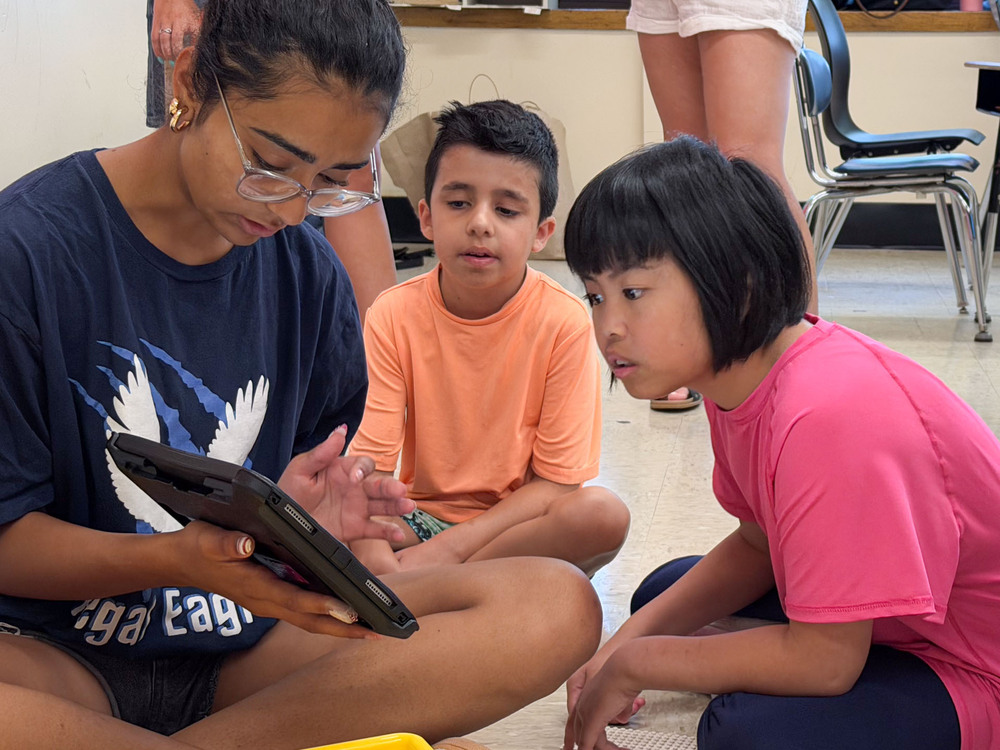 Students sitting on the floor, reading off of tablet.