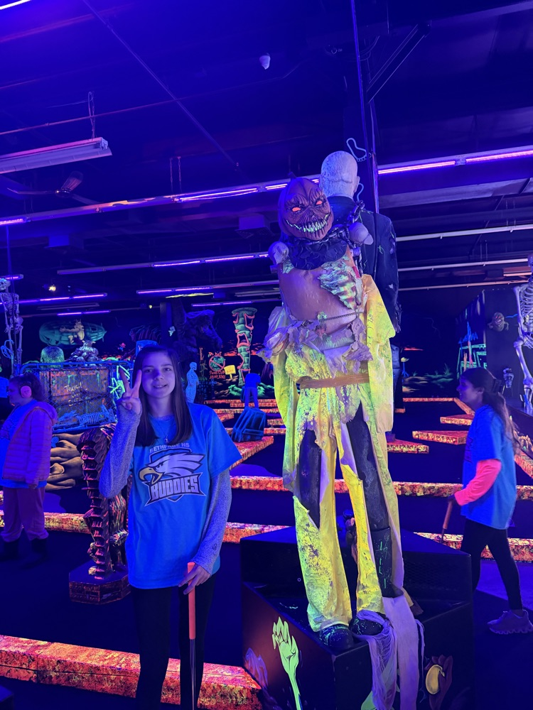 student making piece sign by statue at mini golf