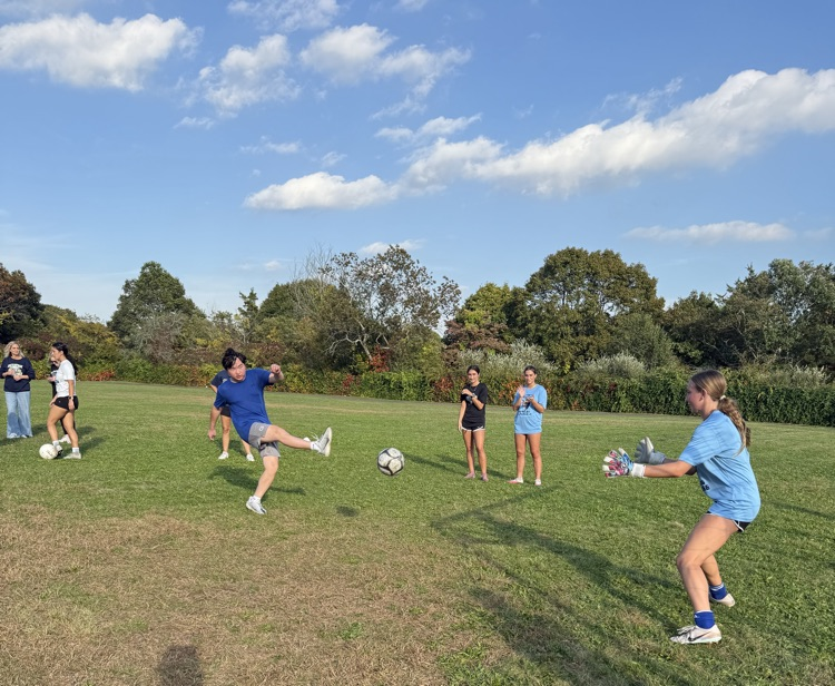 student kicking ball toward goal with goalie trying to stop it