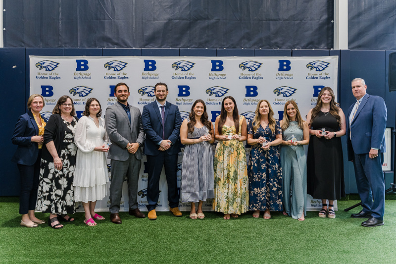 Group photo of award recipients and educators at Bethpage High School's ceremony, celebrating achievements with a backdrop featuring the school's logo.