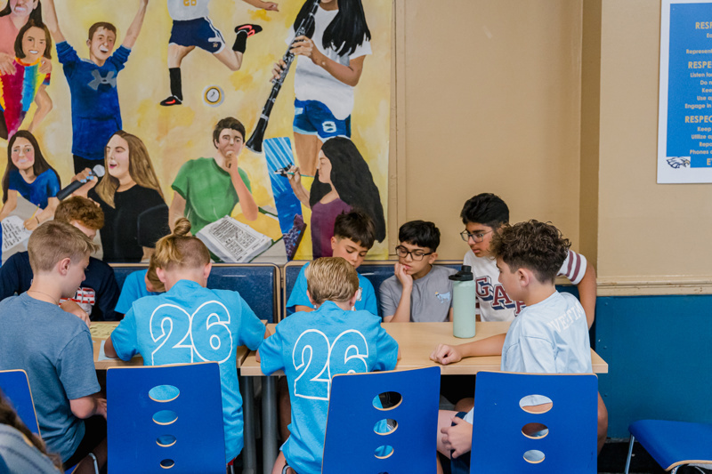 Group of children collaborating at a table in front of a vibrant mural, showcasing teamwork and creativity.
