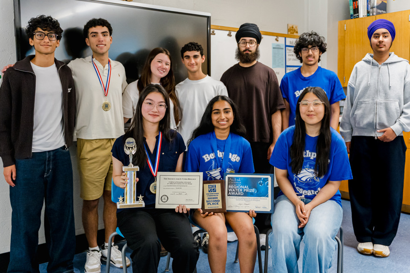 A group of students celebrating academic achievements, holding trophies and certificates, together in a classroom setting.