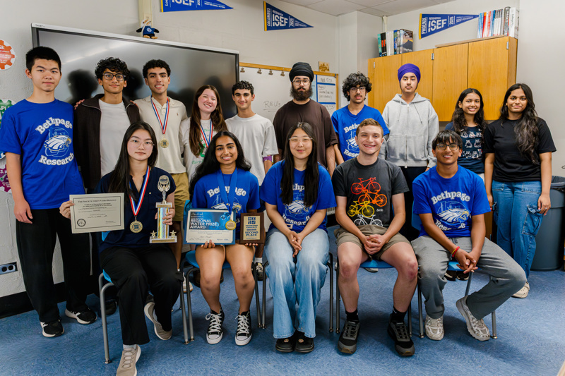 A group of students celebrating academic achievements, holding trophies and certificates, together in a classroom setting.