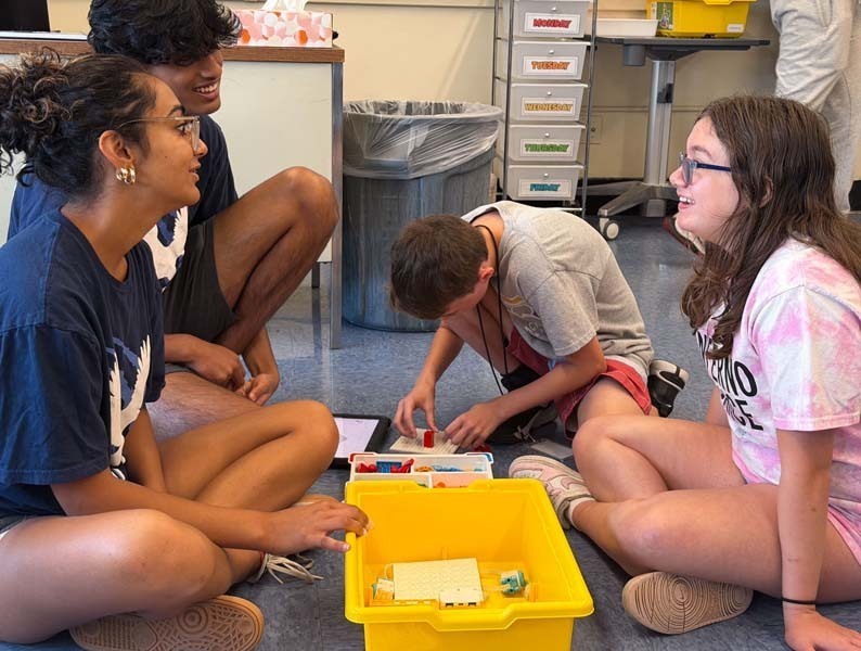 Students sitting on the floor, reading off of tablet.