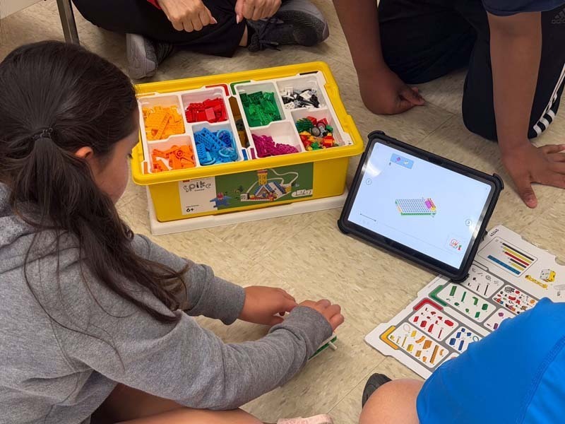 Students sitting on the floor, reading off of tablet.