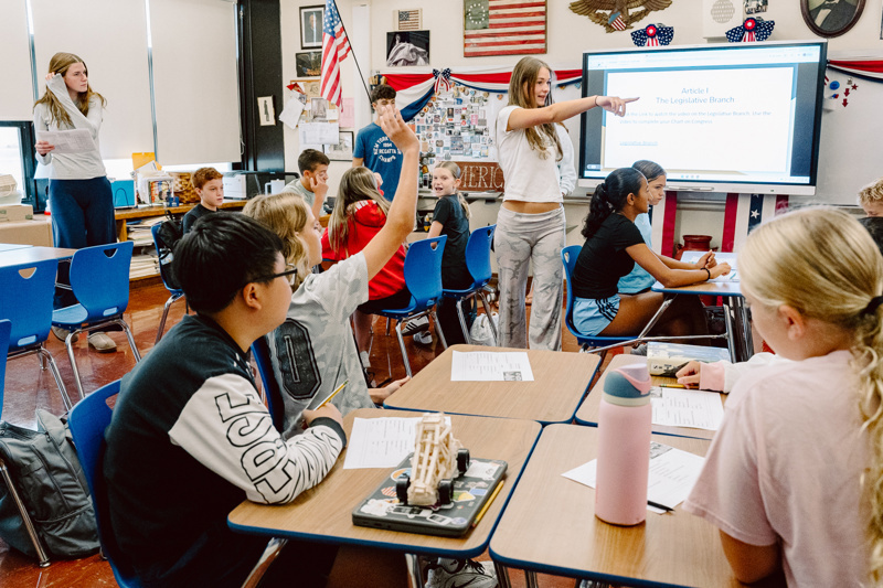 Students engage in a classroom discussion with a presentation displayed on the screen.