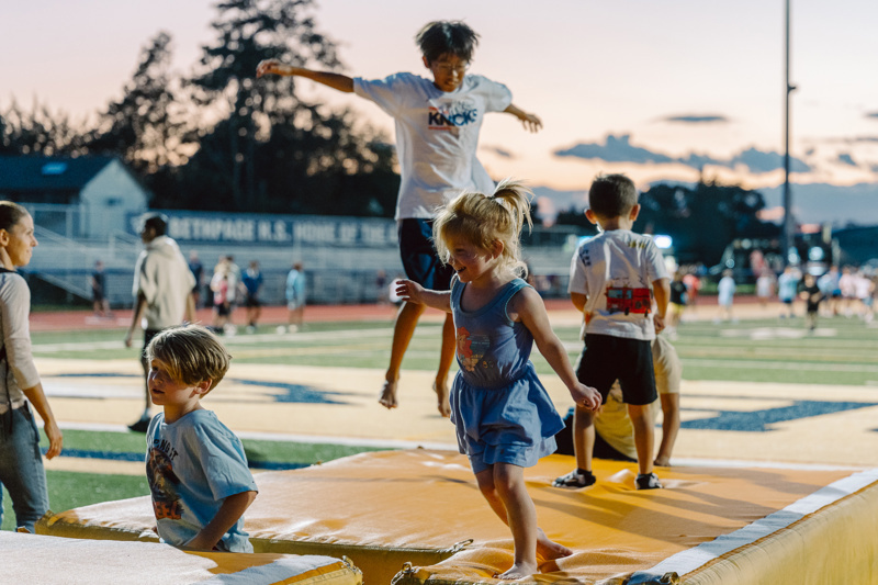 A group of children jumping on a padded surface at an outdoor sports facility.
