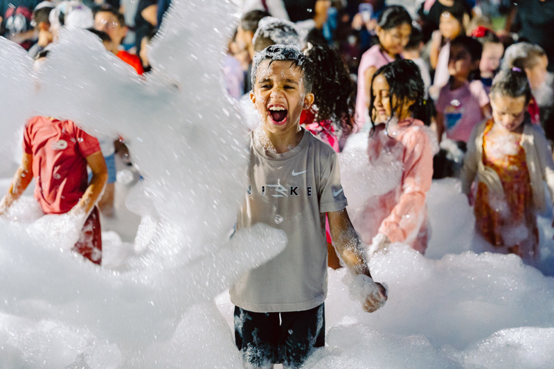 Group of people playing in foam at an outdoor event, with one person in focus.